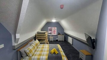 A small, sloped-roofed room with a bed, a desk, a chair, and a window.