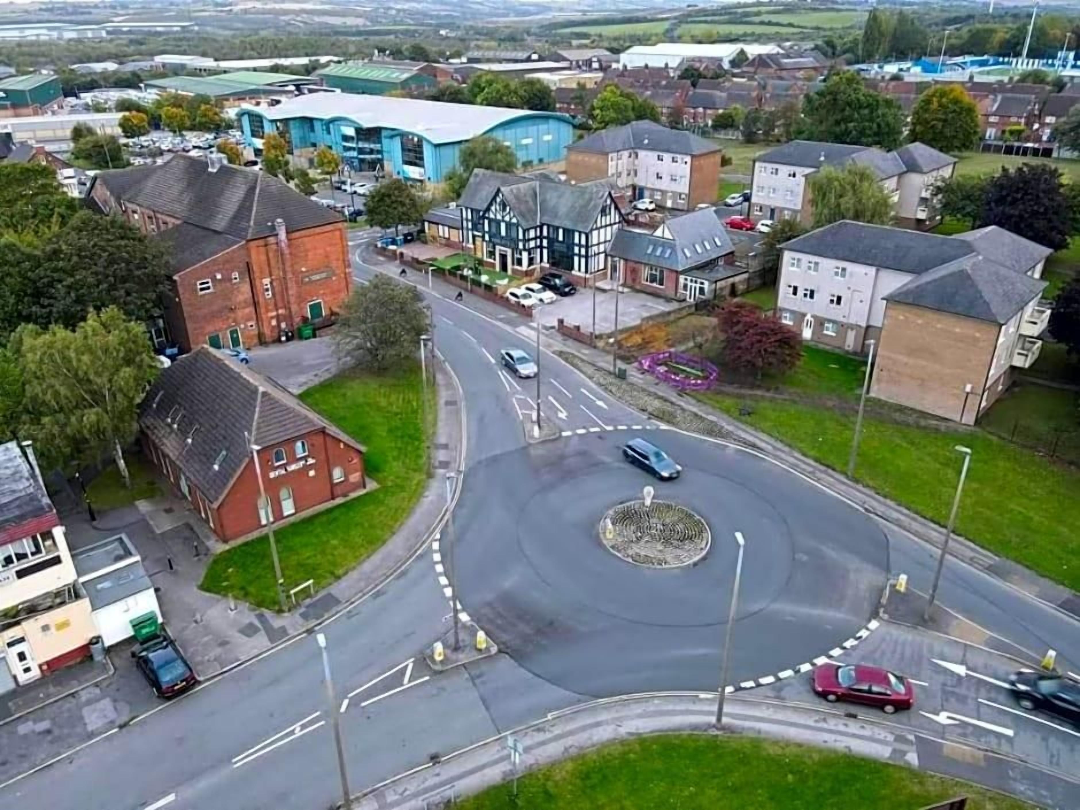 A roundabout with multiple entry and exit points, surrounded by residential buildings and a large industrial facility.