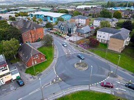 A roundabout with multiple entry and exit points, surrounded by residential buildings and a large industrial facility.