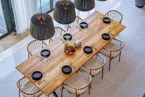 A long wooden dining table with black plates, silverware, and a fruit centerpiece. - Villa Babar Pererenan (Pererenan)