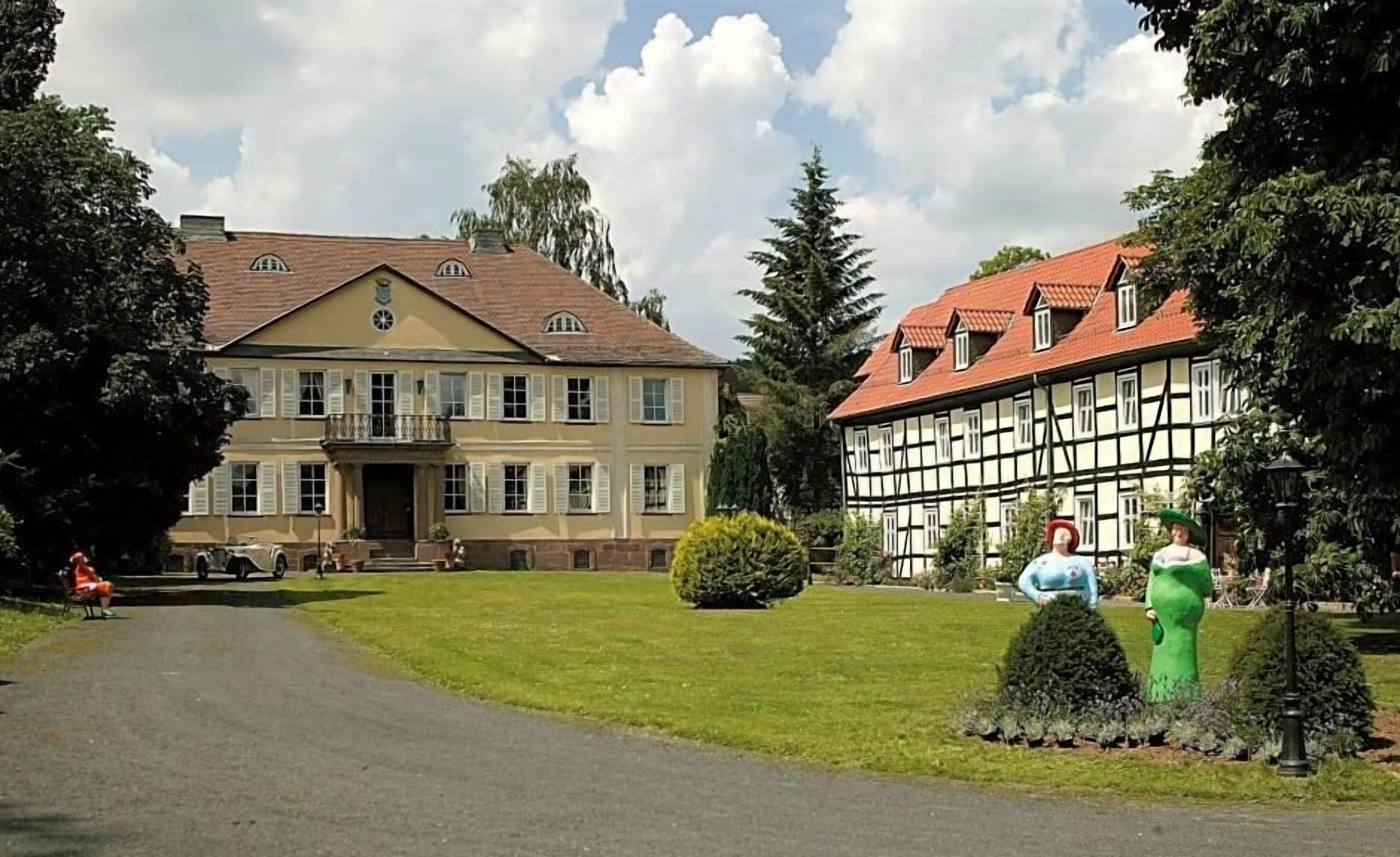 A large building with a symmetrical facade, a central entrance, and a well-maintained lawn with a statue.