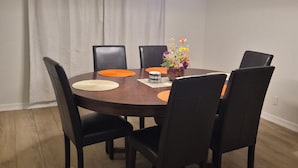 Un'area pranzo con un tavolo rotondo, sei sedie, un vaso con fiori e una lampada a sospensione.