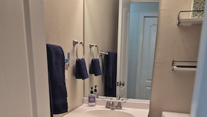 Un bagno con un lavandino bianco, due portasci, uno specchio, un water e un cestino bianco.