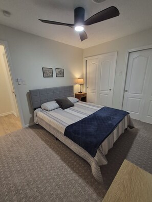 Ein Schlafzimmer mit einem Bett, einem Deckenventilator, einem Nachttisch und einer Tür.