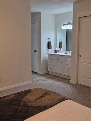A hotel room with a bed, a bathroom with a sink and mirror, and a carpeted floor.