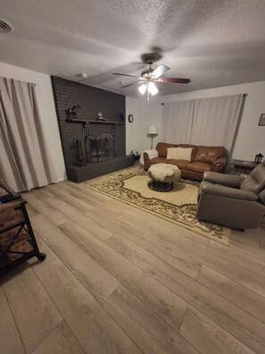 A living room with a fireplace, a ceiling fan, a brown leather sofa, and a patterned rug.