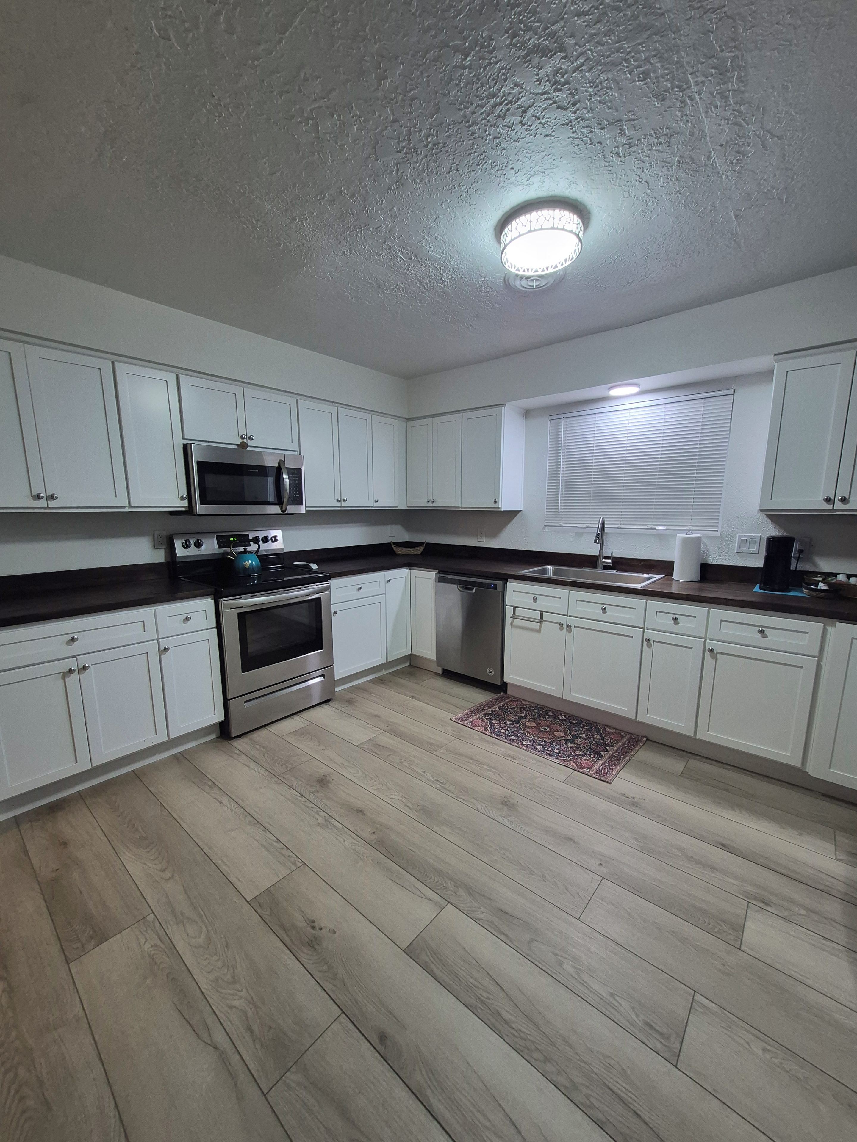 A kitchen with white cabinets, a microwave, stove, dishwasher, and a window with blinds.