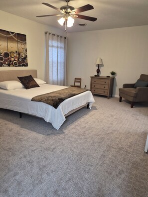 A bedroom with a bed, a ceiling fan, a nightstand, a chair, and a painting on the wall.
