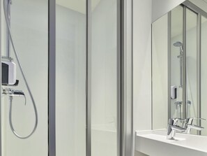 Un baño moderno con cabina de ducha de vidrio, ducha de mano y grifo empotrado.