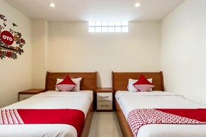 Habitación de hotel con dos camas, cada una con cabecero de madera, ropa de cama blanca y almohadas rojas. Hay una ventana pequeña sobre las camas y una decoración en la pared con la palabra 'OYO'.
