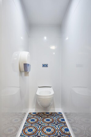 Um banheiro pequeno e moderno, com vaso sanitário, secador de mãos e piso estampado.