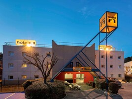 Un hotel de diseño moderno, con un llamativo letrero 'hotel F1', entrada roja y zona de estacionamiento.