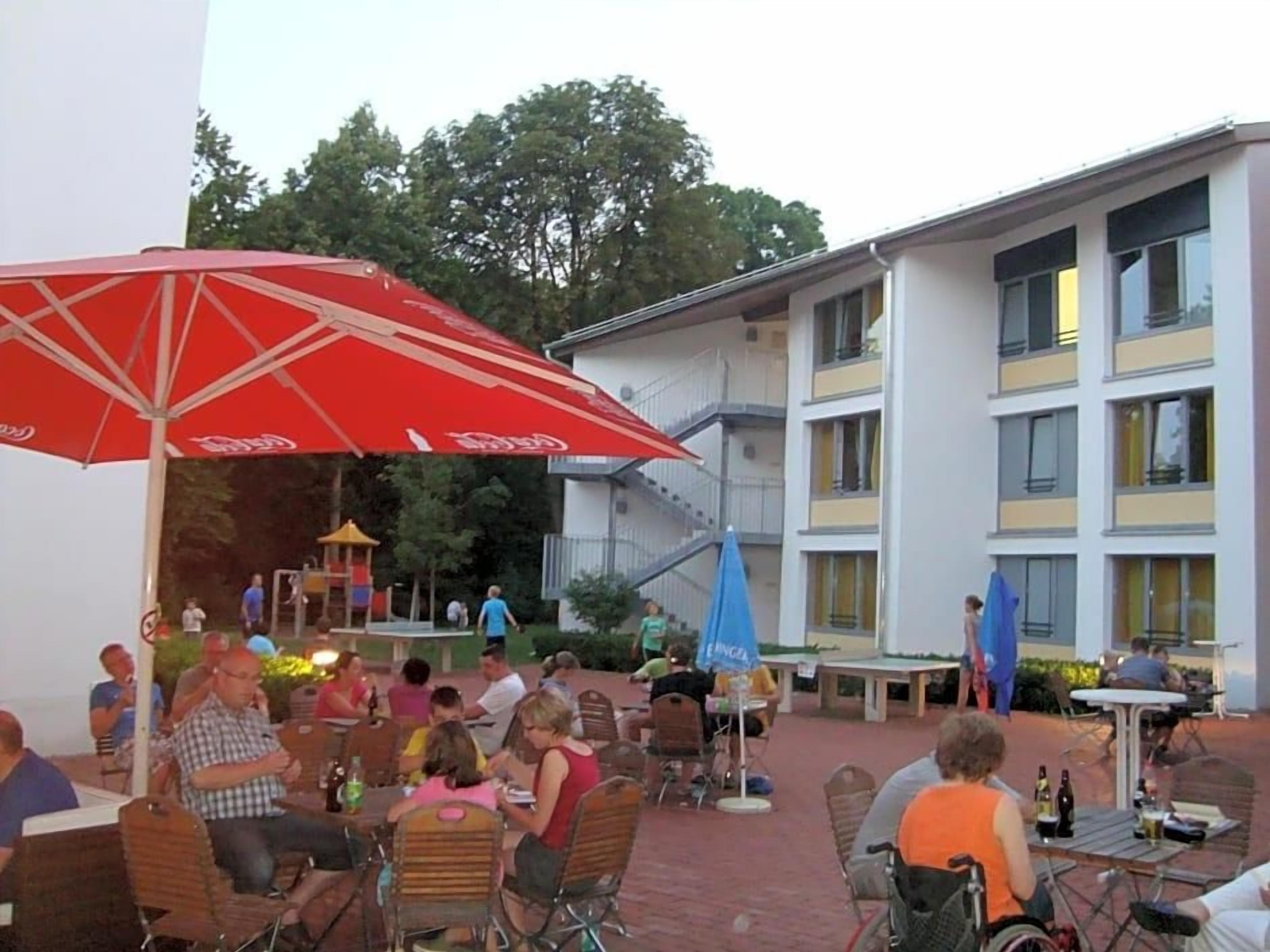 An outdoor seating area with tables and chairs, umbrellas, and a building in the background.