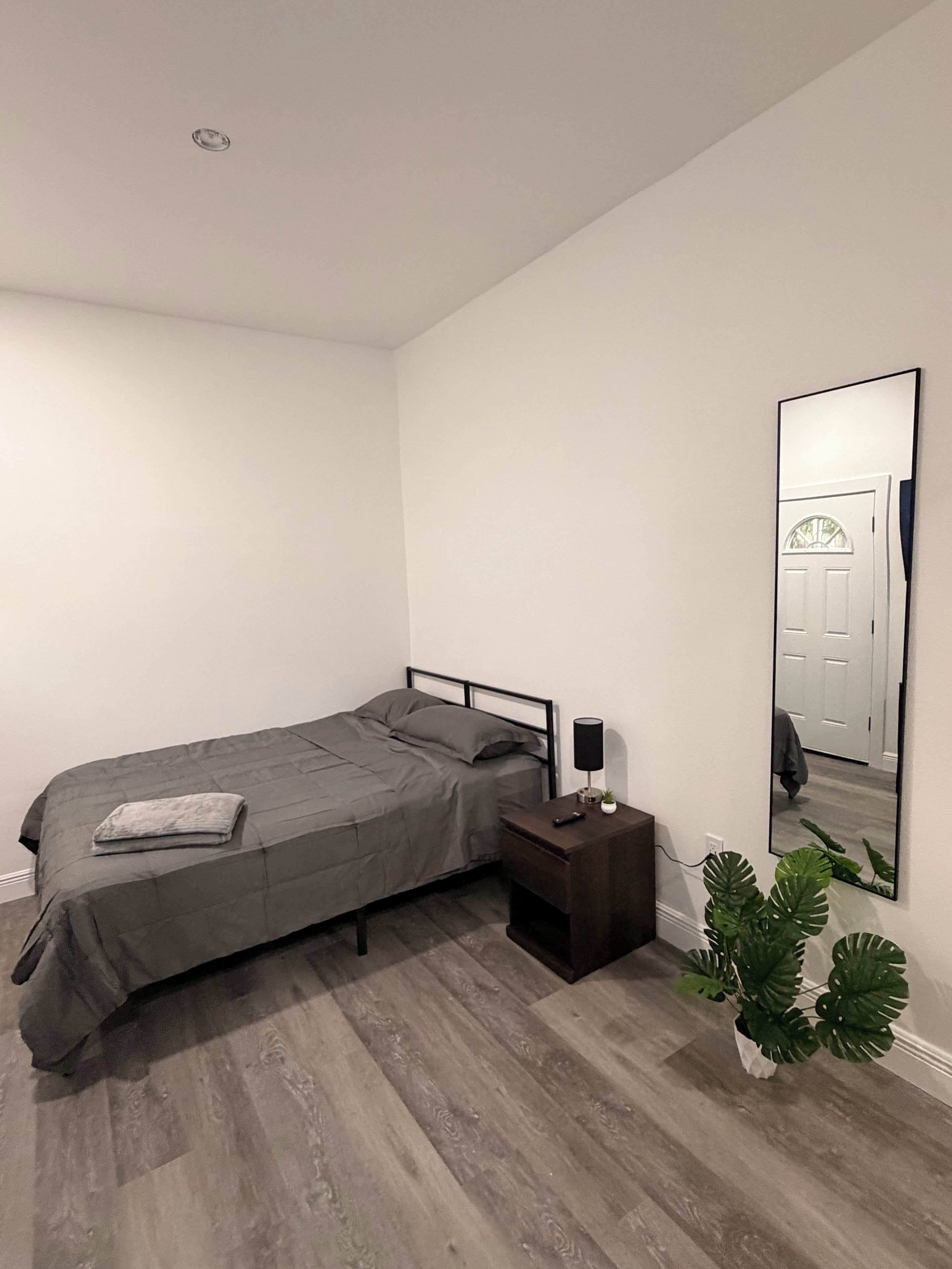 Ein Schlafzimmer mit einem Bett, einem Nachttisch, einer Lampe und einem großen Spiegel an der Wand.