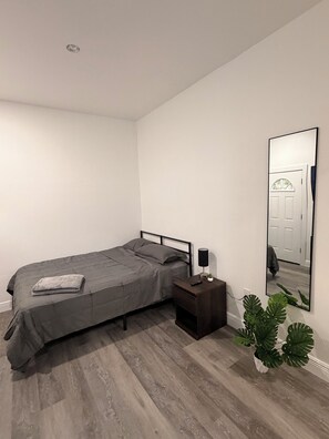 Ein Schlafzimmer mit einem Bett, einem Nachttisch, einer Lampe und einem großen Spiegel an der Wand.