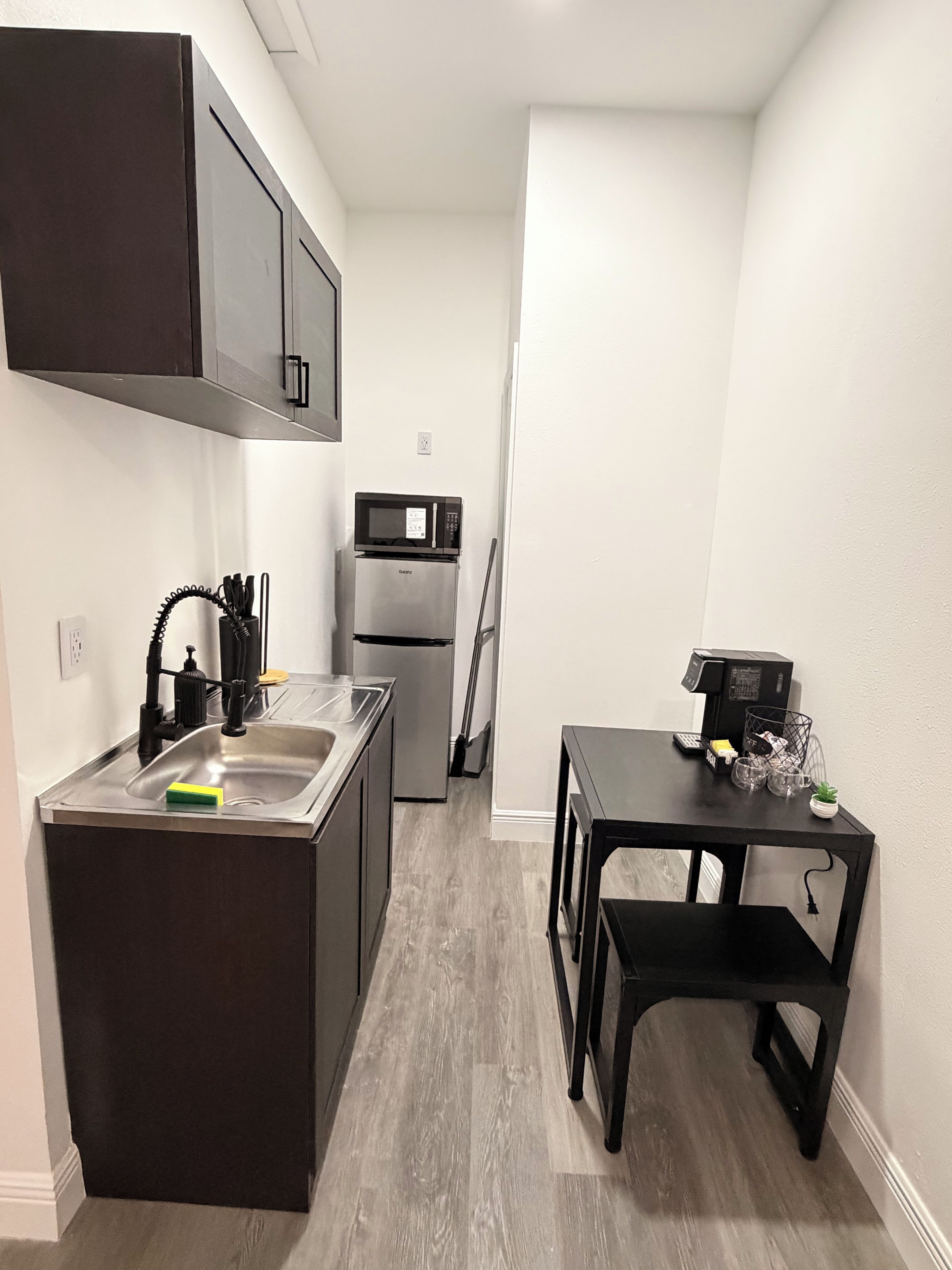 Una cocina funcional con un lavamanos, microondas, refrigerador y una mesa de comedor.