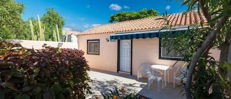 A small building with a tiled roof, a white door, and a patio with white chairs and a table.