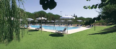A swimming pool with lounge chairs and umbrellas, surrounded by a well-maintained lawn and trees.