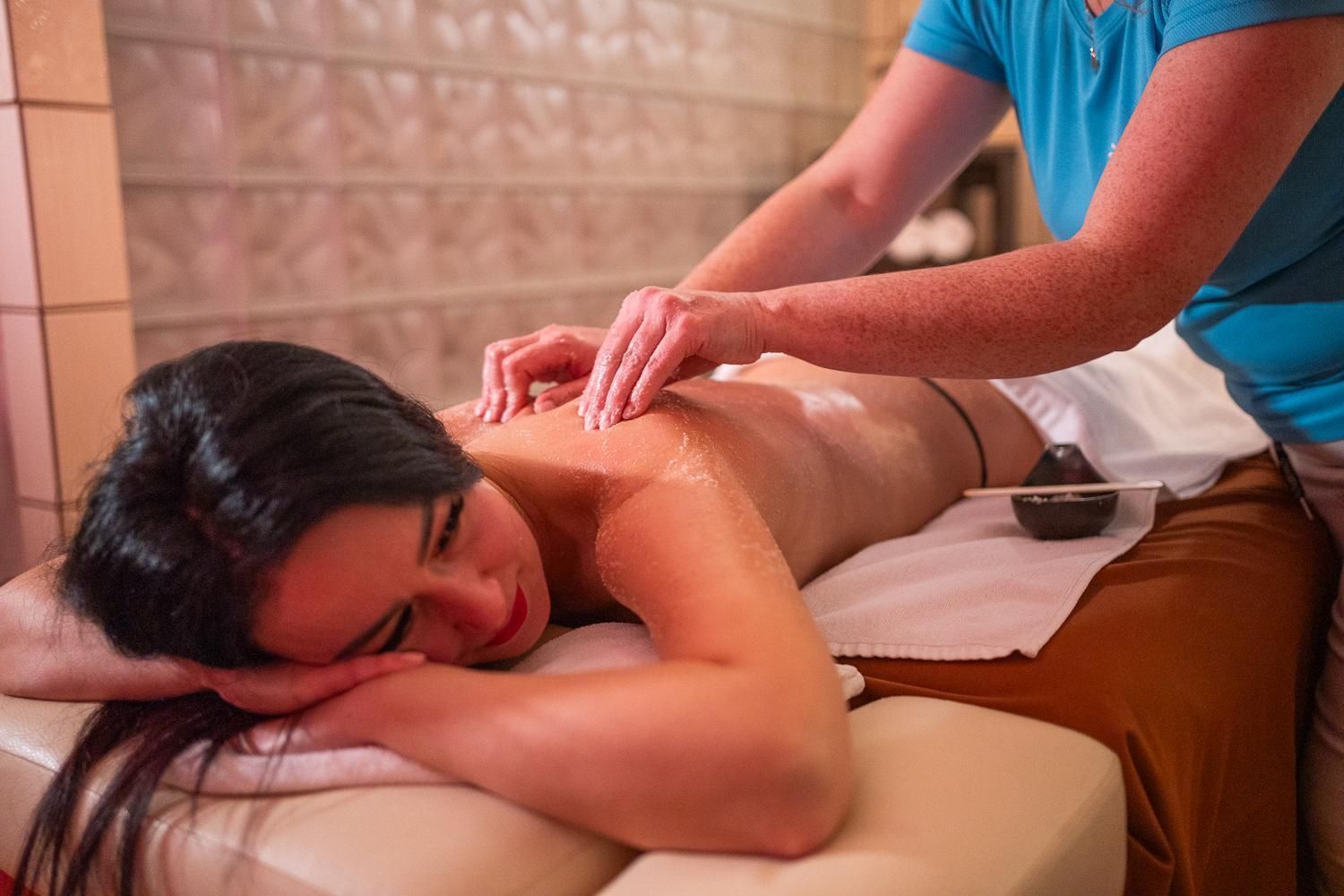 Eine Person bekommt eine Massage in einem Raum mit gefliesten Wänden und einer Massageliege.