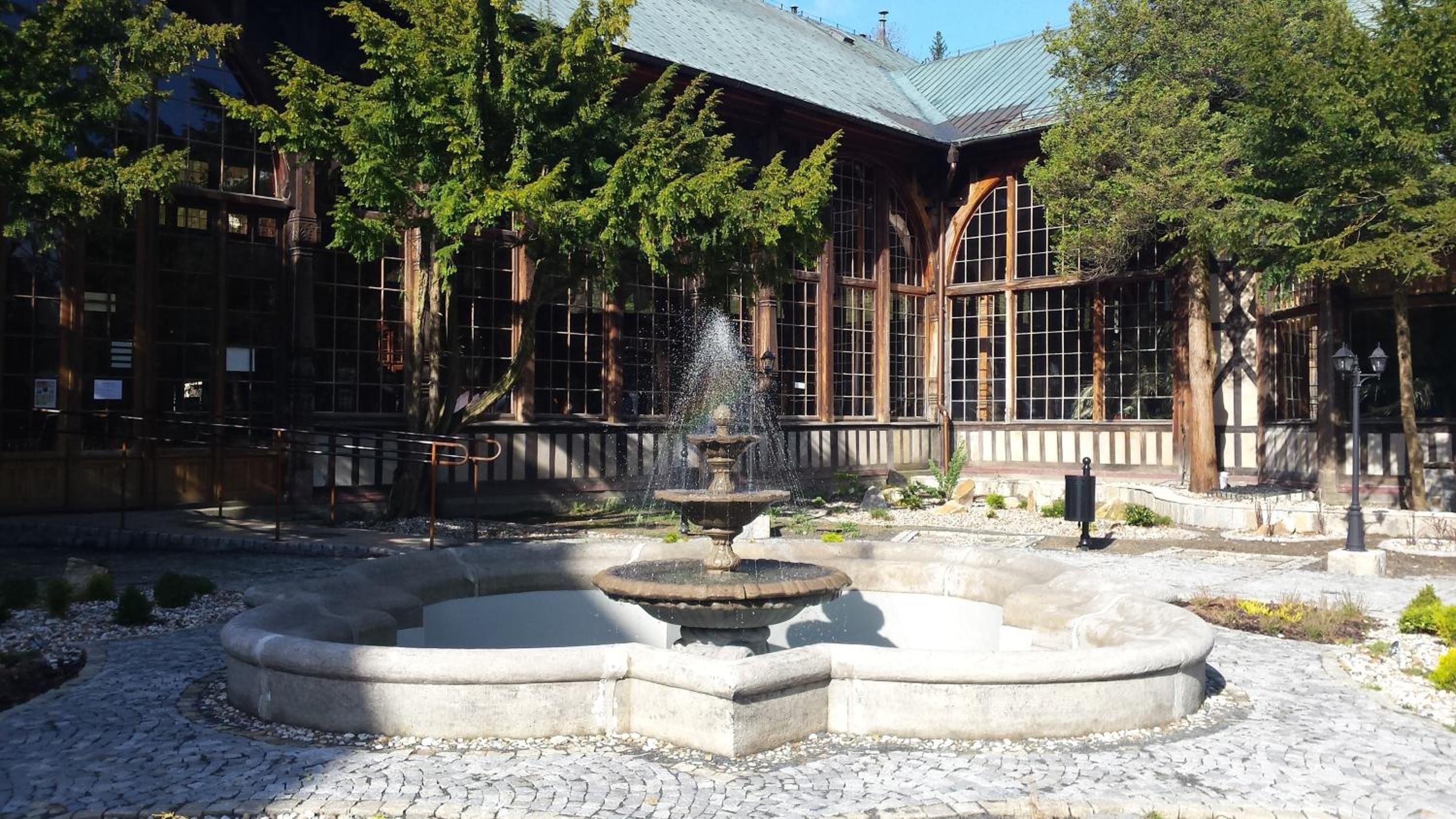 Un patio con una fuente, un sendero de piedra y un edificio con ventanas grandes y vigas de madera.
