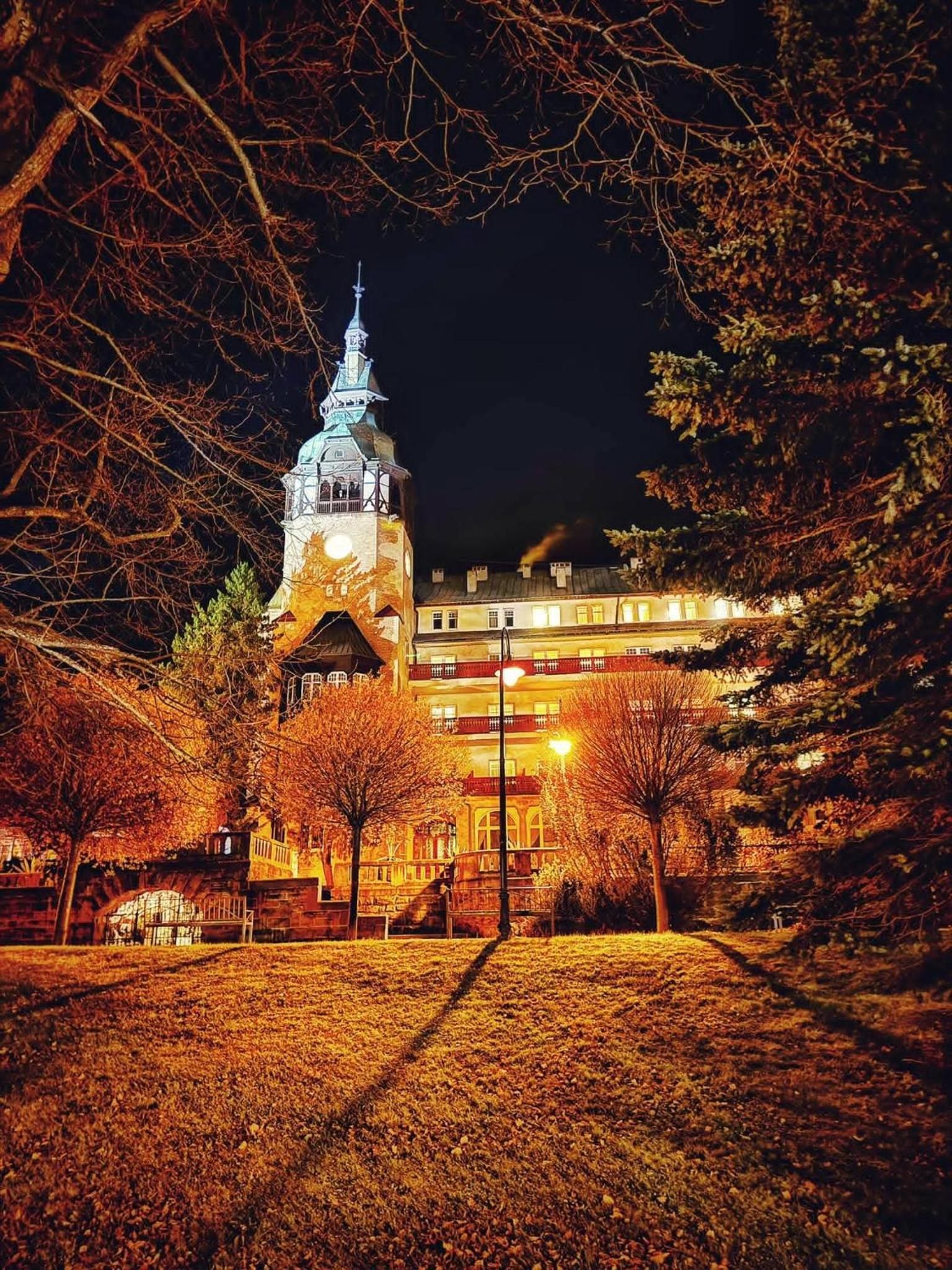 Ein historisches Gebäude mit einem markanten Turm und einer Uhr, umgeben von Bäumen und beleuchtet von Straßenlaternen.