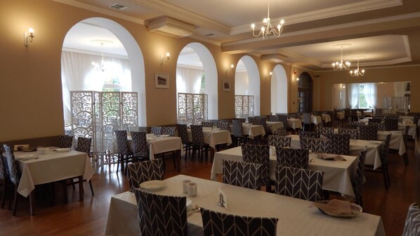 Un restaurante con varias mesas y sillas, ventanas en arco e iluminación decorativa.