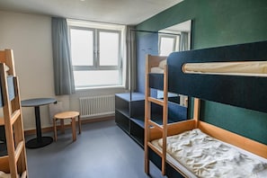 A compact room with bunk beds, a small table, and a radiator.