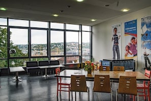 A spacious indoor area with large windows, a seating area with tables and chairs, and a foosball table.