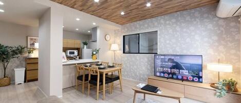 Una sala moderna con techo de madera, televisor de pantalla plana, comedor y cocina al fondo.