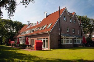 A two-story brick building with a sloped roof, multiple windows, and a red door.