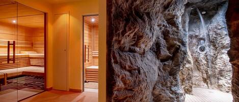 A spa room with wooden benches and a stone wall with a water feature.