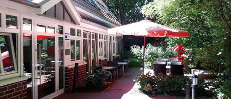 An outdoor patio area with tables and chairs, a red umbrella, and a brick wall.