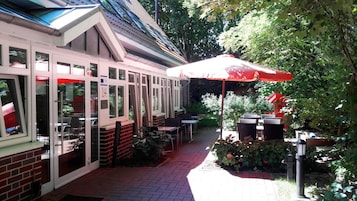 An outdoor patio area with tables and chairs, a red umbrella, and a brick wall.