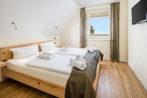 Habitación de hotel con una cama grande, una mesita de noche, una ventana con cortinas y un televisor de pantalla plana montado en la pared.