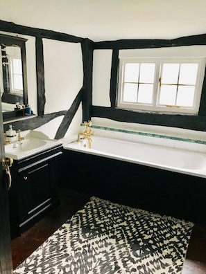 A bathroom with a white bathtub, a black and white patterned rug, and a window with white panes. - Oldlands Farm Bed and Breakfast (Crawley)