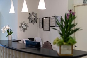 Una recepción con una orquídea en maceta, documentos enmarcados en la pared y una puerta con un cartel arriba.