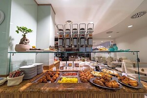 Un'area buffet con diverse opzioni alimentari, un angolo caffè e una zona salotto con tavoli e sedie.