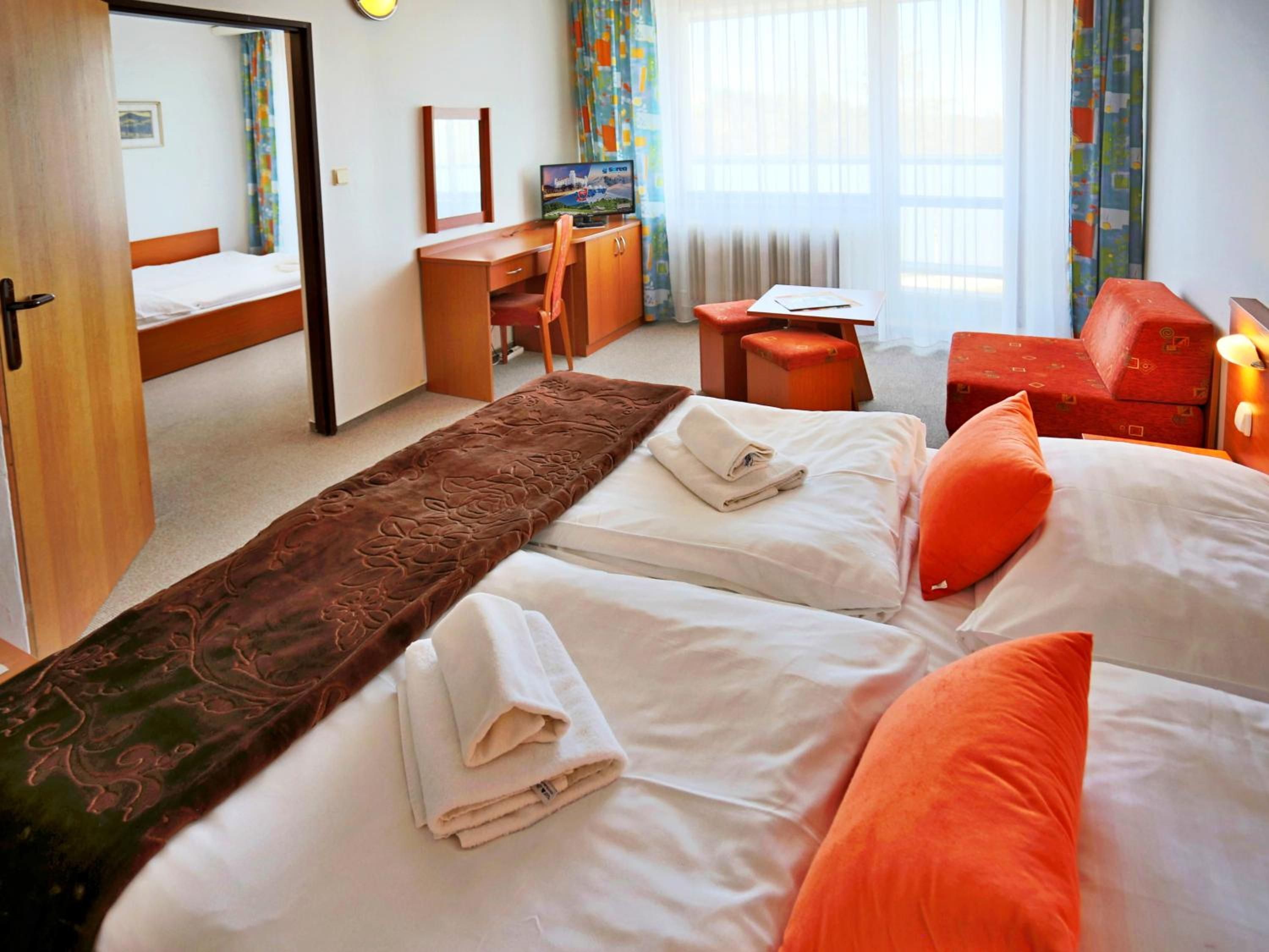 A hotel room with two beds, a desk, a television, and a window with curtains.