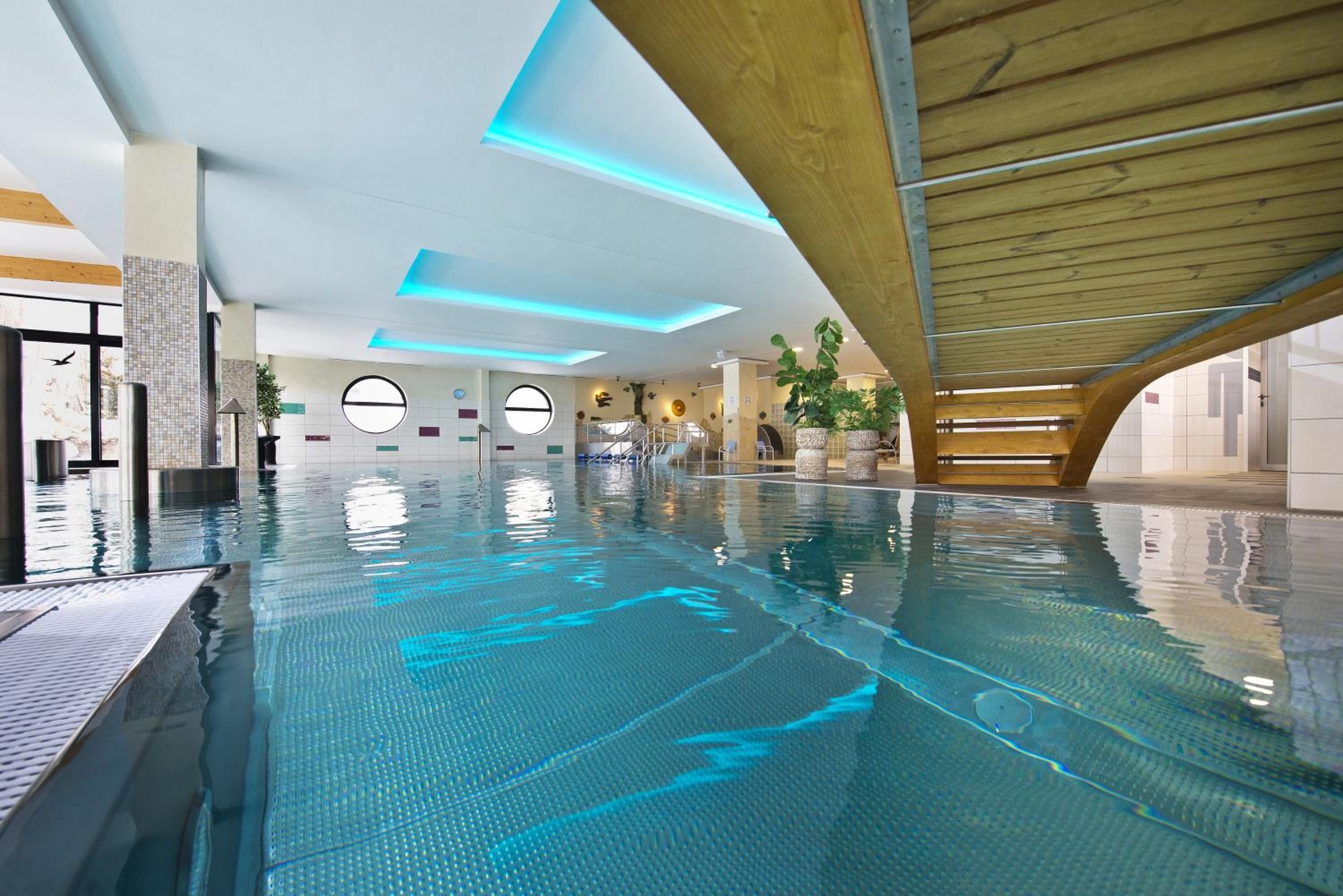 Una piscina interior con diseño moderno, que presenta una estructura de techo de madera y ventanas circulares.