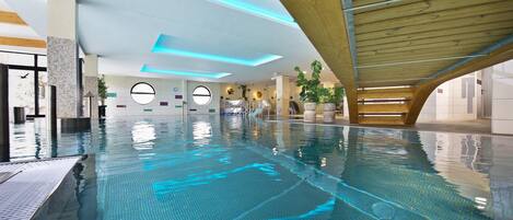 Una piscina interior con diseño moderno, que presenta una estructura de techo de madera y ventanas circulares.