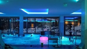 Una piscina con una luce rosa galleggiante, circondata da pareti in vetro e vista su un paesaggio innevato.