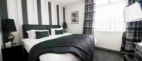 Habitación de hotel con cama, mesita de noche, lámpara, un cuadro en la pared y ventana con cortinas.