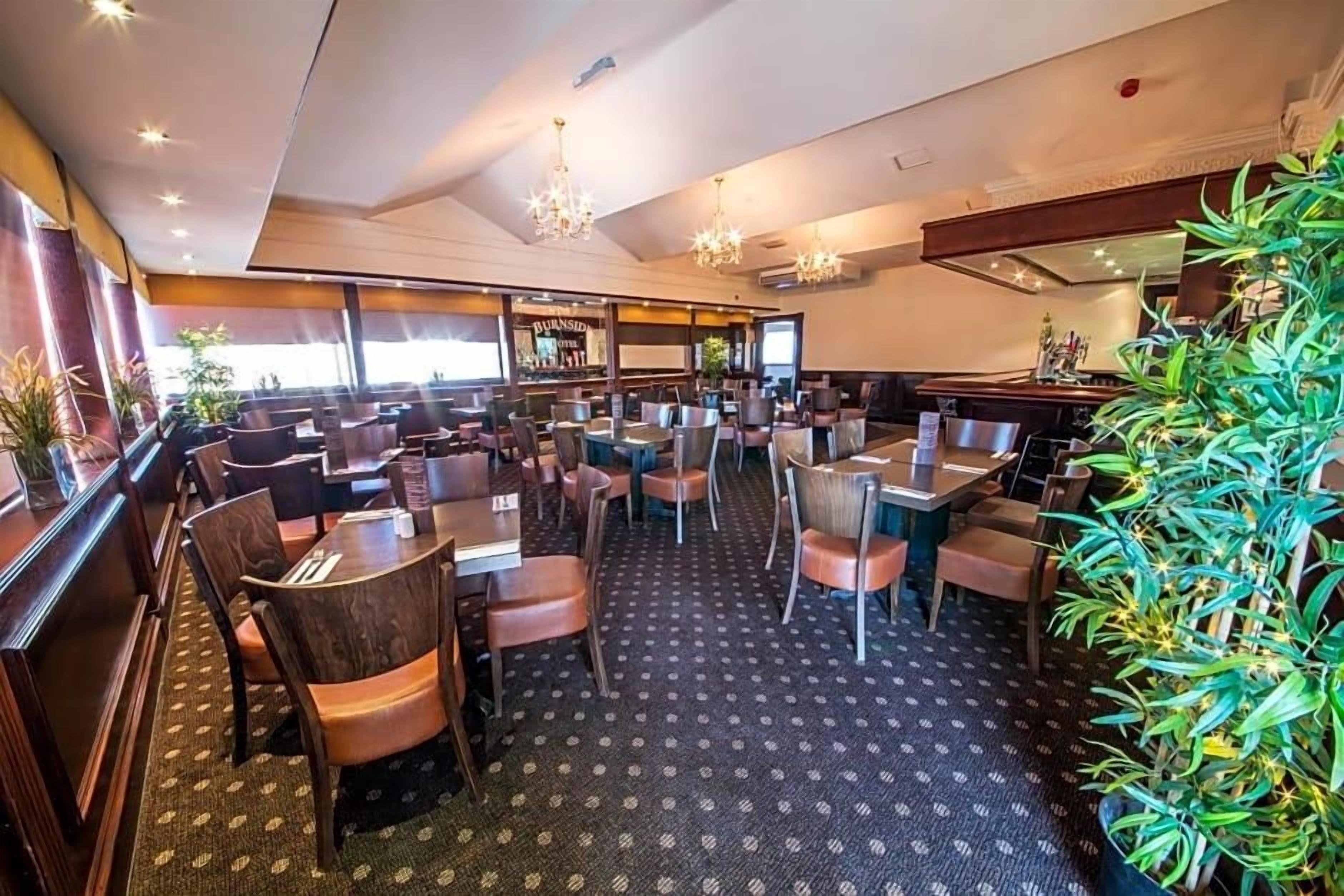Un restaurante con varias mesas y sillas, una zona de bar y una alfombra estampada.