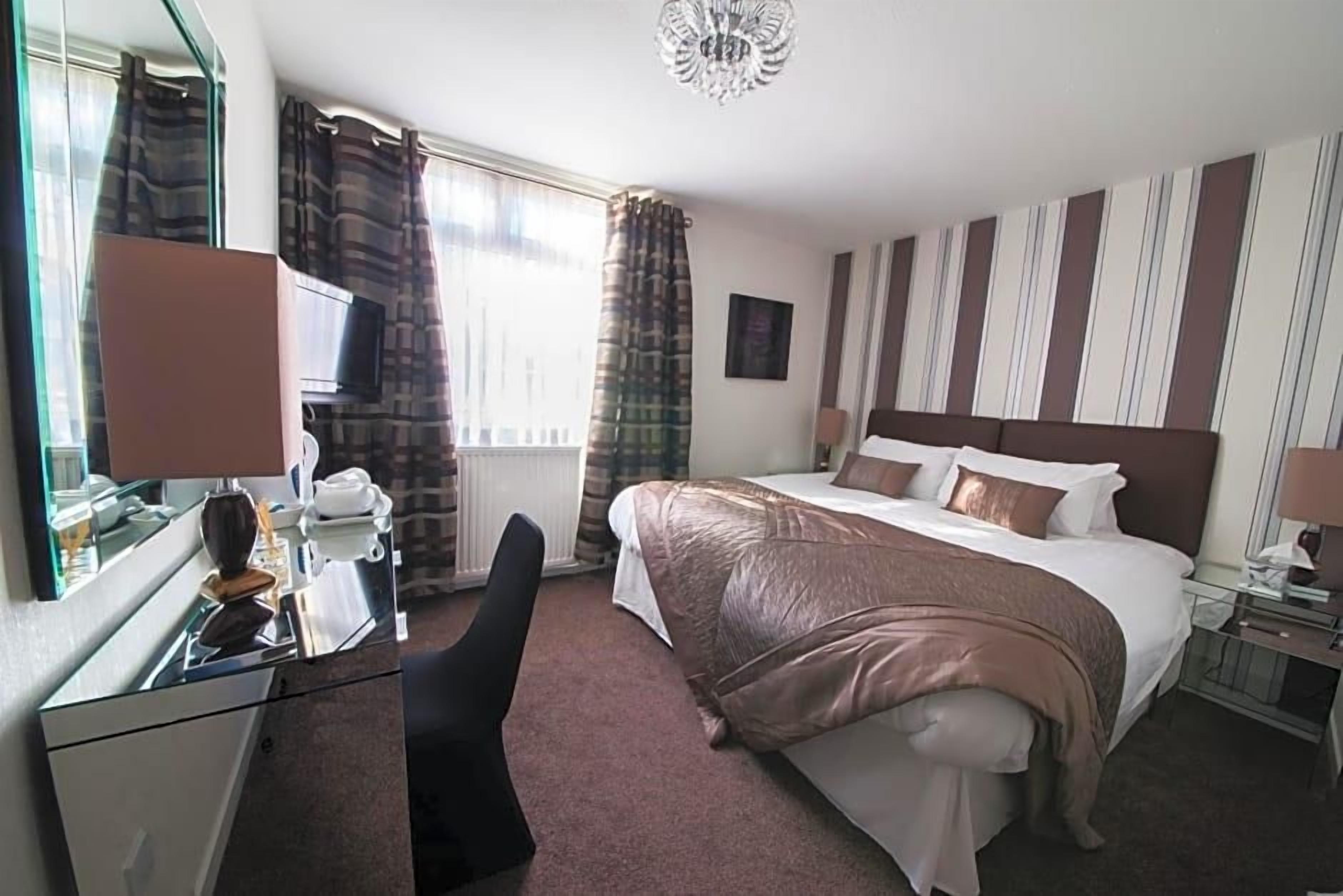 Een hotelkamer met een bed, een bureau, een stoel, een televisie en een raam met gordijnen.