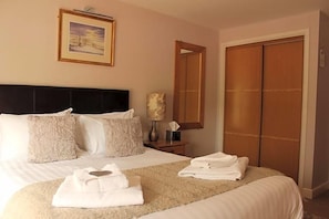 A hotel room with a bed, pillows, a bedside table with a lamp, a mirror, and a wardrobe.