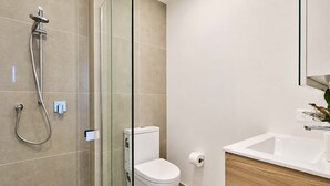 Une salle de bain moderne avec une douche à parois de verre, des toilettes blanches et un meuble-lavabo en bois avec un évier.