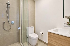 A modern bathroom with a glass-enclosed shower, a white toilet, and a wooden vanity with a sink. - Wellington City Stay - 1BR with Pool & Gym (Wellington)