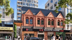 Un bâtiment à la façade en briques, avec les devantures des magasins TJ Katsu et Majestic Cuisine, et un immeuble moderne en arrière-plan.