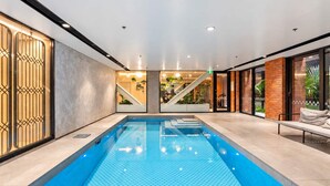 Une piscine intérieure moderne, dotée d’une eau cristalline, et entourée d’un décor minimaliste agrémenté d’un escalier et d’un espace détente.