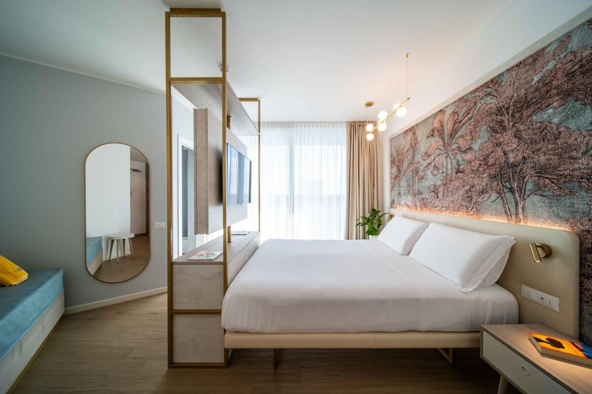 Una habitación de hotel moderna con una cama grande, una mesita de noche, un espejo y un televisor montado en la pared.